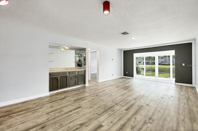 unfurnished living room with a textured ceiling, light wood finished floors, visible vents, and baseboards