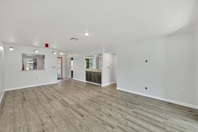 unfurnished living room with light wood-type flooring, visible vents, a textured ceiling, and baseboards