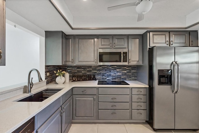 kitchen featuring light tile patterned floors, stainless steel appliances, gray cabinets, decorative backsplash, and a sink