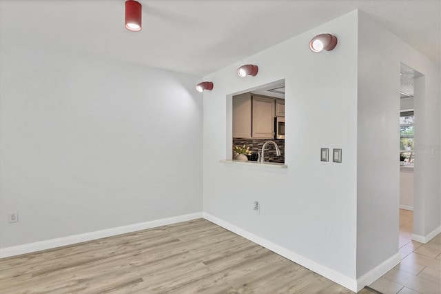 empty room with light wood finished floors, a sink, and baseboards