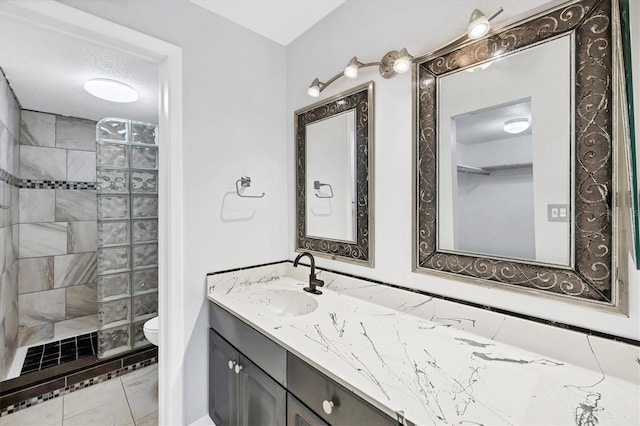 full bath with toilet, a textured ceiling, tiled shower, and vanity