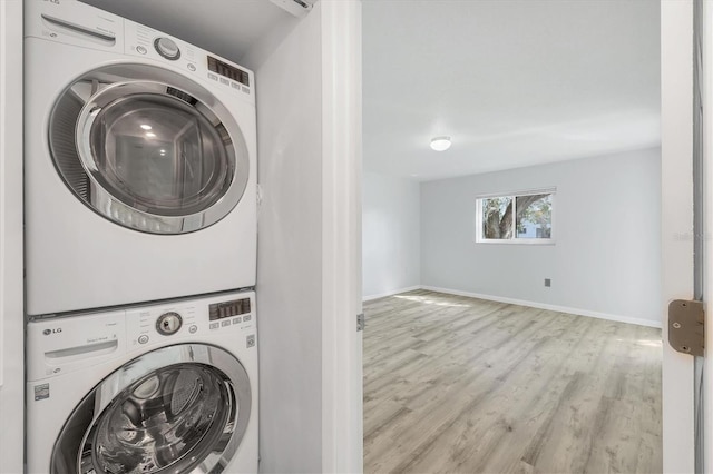 laundry area featuring baseboards, laundry area, wood finished floors, and stacked washer / drying machine