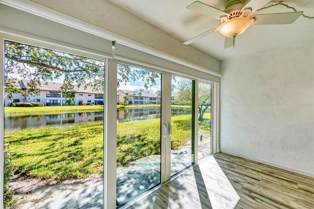 entryway featuring ceiling fan, a textured wall, a water view, wood finished floors, and baseboards