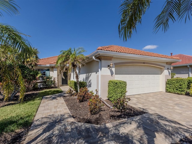 mediterranean / spanish house with a garage, driveway, a tile roof, and stucco siding