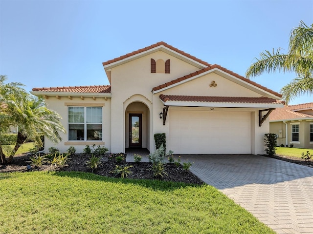 mediterranean / spanish-style house with a garage, decorative driveway, a front lawn, and stucco siding