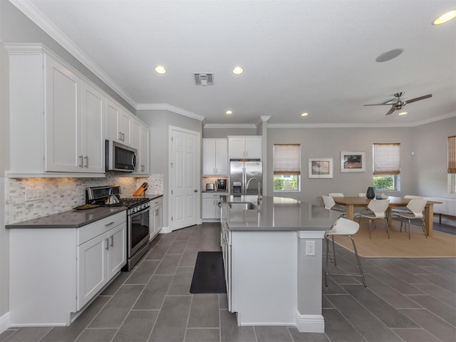 kitchen with a center island with sink, stainless steel appliances, tasteful backsplash, visible vents, and a sink