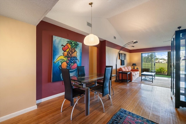 dining space with lofted ceiling, wood finished floors, visible vents, and baseboards