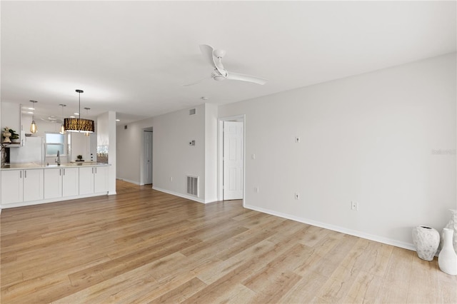 unfurnished living room featuring light wood-style flooring, a sink, visible vents, baseboards, and a ceiling fan