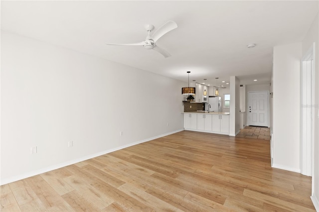 unfurnished living room featuring ceiling fan, baseboards, a sink, and light wood-style floors