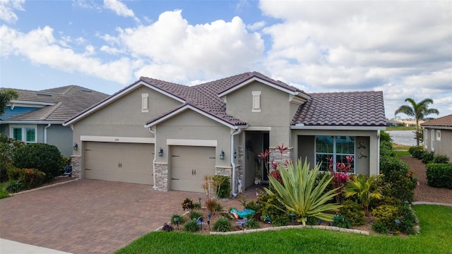 mediterranean / spanish house featuring decorative driveway, a tile roof, stucco siding, an attached garage, and stone siding