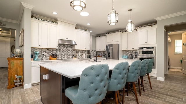 kitchen featuring light countertops, appliances with stainless steel finishes, ornamental molding, a sink, and under cabinet range hood