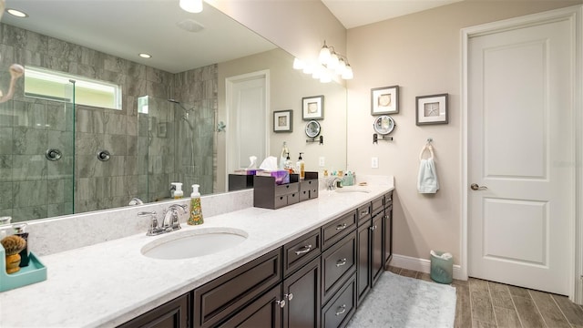 bathroom with double vanity, wood finish floors, a sink, and tiled shower