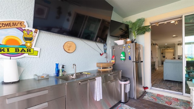 kitchen featuring a textured wall, brick floor, a sink, and freestanding refrigerator