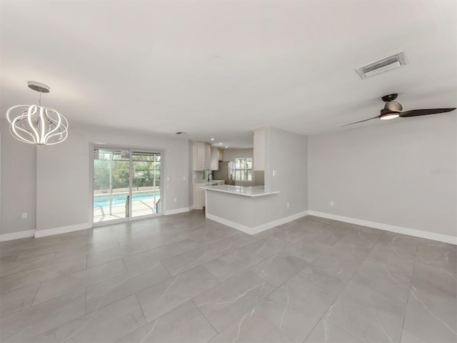 unfurnished living room featuring ceiling fan with notable chandelier, visible vents, and baseboards