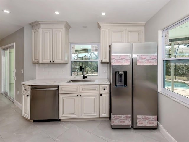 kitchen featuring appliances with stainless steel finishes, white cabinetry, a sink, and light stone counters