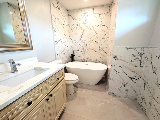 full bath featuring marble finish floor, a freestanding bath, toilet, vanity, and stone wall