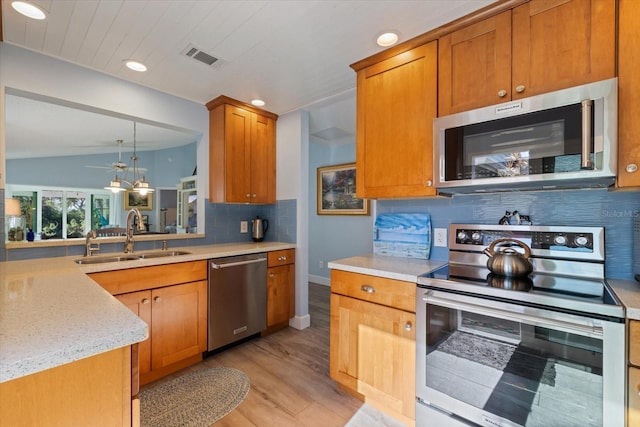 kitchen featuring brown cabinets, stainless steel appliances, backsplash, a sink, and light wood-type flooring