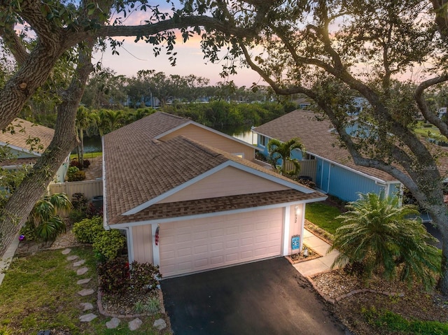 exterior space with a garage, roof with shingles, driveway, and fence