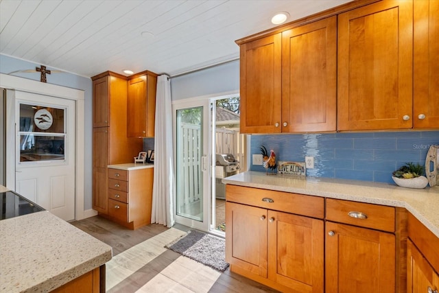 kitchen featuring light wood-type flooring, light stone countertops, brown cabinetry, and decorative backsplash