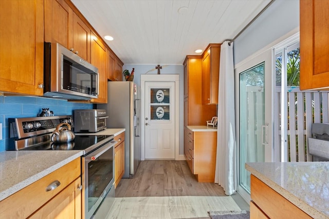 kitchen featuring a toaster, appliances with stainless steel finishes, brown cabinetry, and decorative backsplash