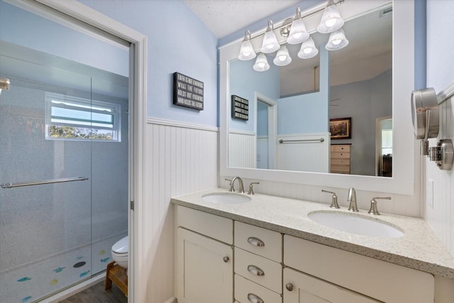 bathroom featuring a wainscoted wall, a sink, toilet, and a shower stall