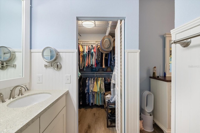 bathroom featuring a spacious closet, vanity, wood finished floors, and wainscoting