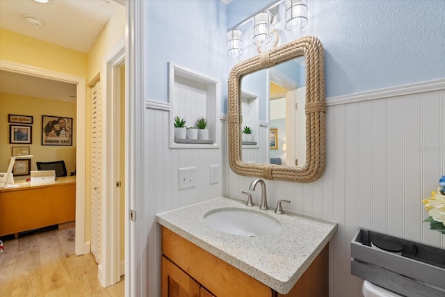 bathroom with a wainscoted wall, vanity, and wood finished floors