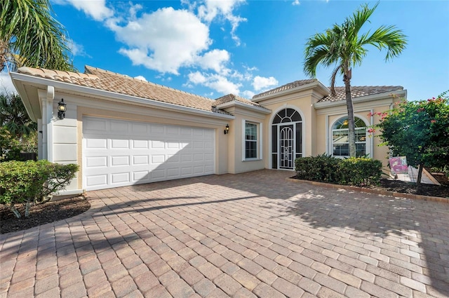 mediterranean / spanish house with decorative driveway, a tiled roof, an attached garage, and stucco siding