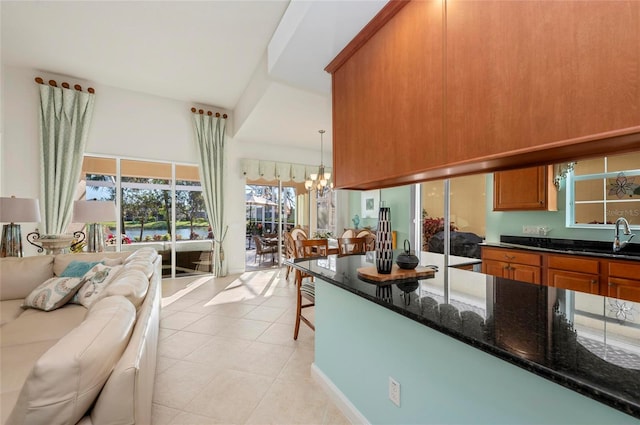 kitchen with brown cabinetry, dark stone counters, open floor plan, a chandelier, and a sink