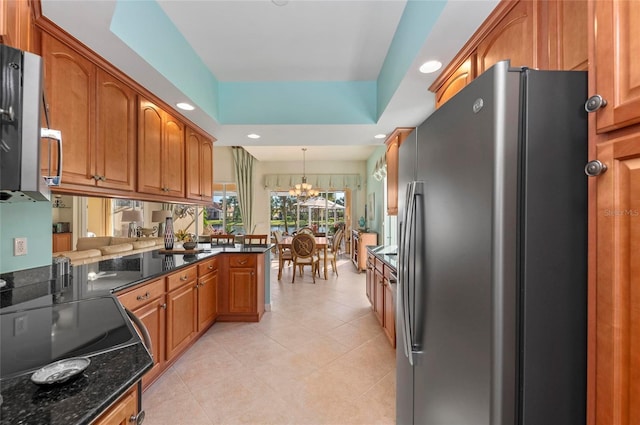 kitchen with freestanding refrigerator, brown cabinets, dark stone countertops, a raised ceiling, and decorative light fixtures