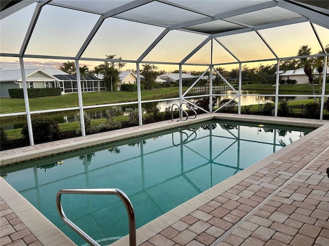 pool at dusk featuring a patio area, a lanai, a water view, and an outdoor pool