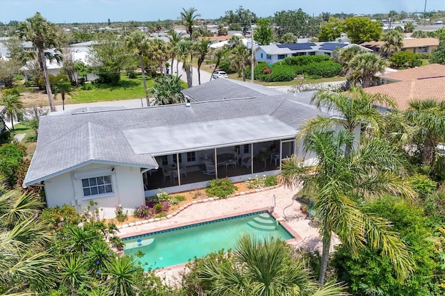 back of property featuring a sunroom, a shingled roof, an outdoor pool, and stucco siding