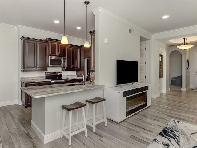 kitchen with arched walkways, a sink, light wood-style floors, dark brown cabinets, and appliances with stainless steel finishes