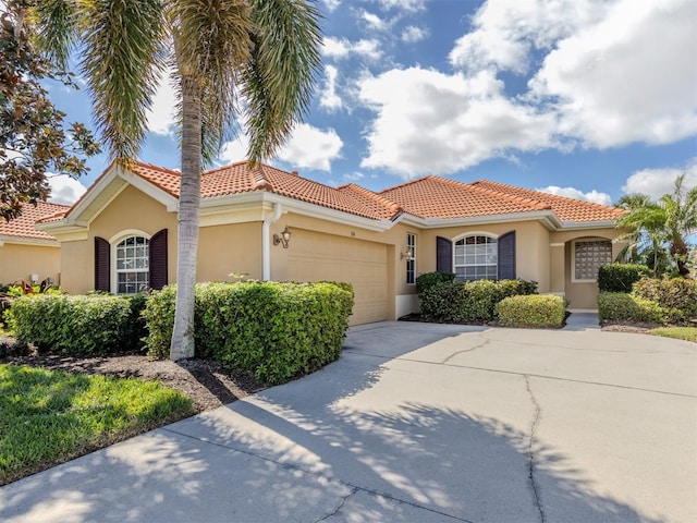 mediterranean / spanish home featuring a garage, concrete driveway, a tile roof, and stucco siding