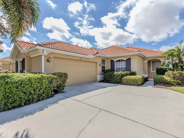 mediterranean / spanish-style home with a garage, driveway, a tile roof, and stucco siding