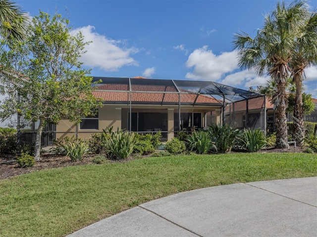 back of house featuring a yard, a tile roof, a lanai, and stucco siding