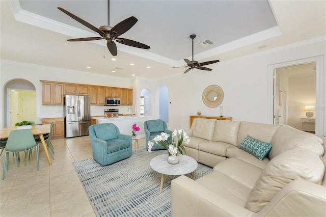 living area featuring light tile patterned floors, crown molding, arched walkways, and a tray ceiling