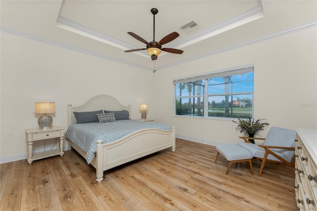 bedroom featuring light wood-style floors, a raised ceiling, visible vents, and crown molding