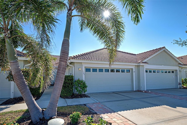 ranch-style house featuring a garage, a tile roof, concrete driveway, and stucco siding