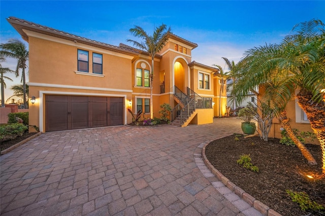 mediterranean / spanish house featuring an attached garage, stairway, decorative driveway, and stucco siding