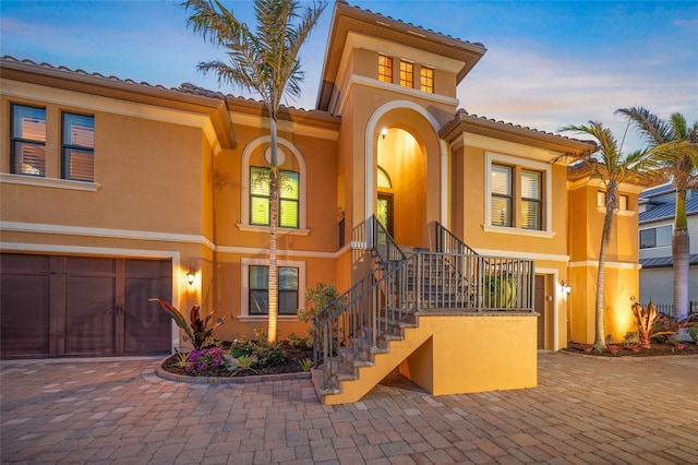 mediterranean / spanish house featuring stairs, decorative driveway, a garage, and stucco siding