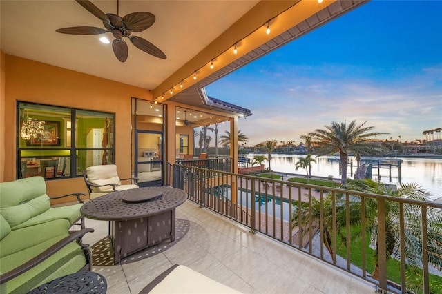 balcony at dusk with a water view and ceiling fan