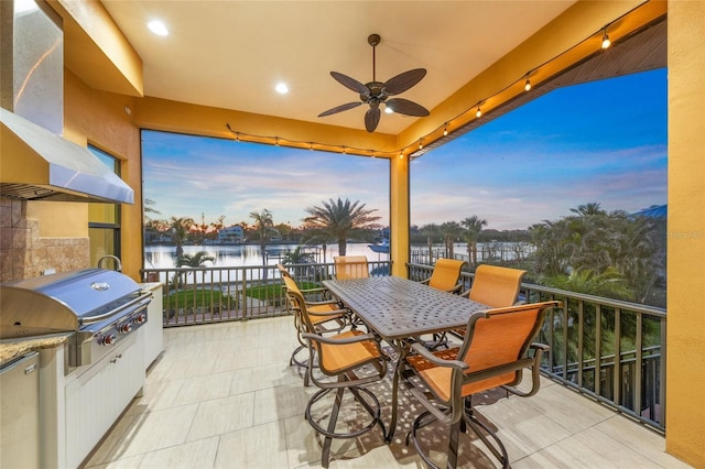 patio terrace at dusk featuring an outdoor kitchen, a ceiling fan, area for grilling, a water view, and outdoor dining area