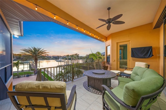 balcony at dusk with a water view, ceiling fan, and outdoor lounge area