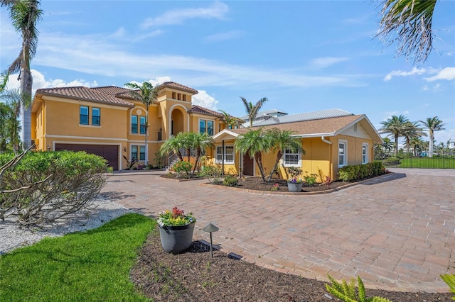 mediterranean / spanish-style house with an attached garage, fence, a tile roof, decorative driveway, and stucco siding