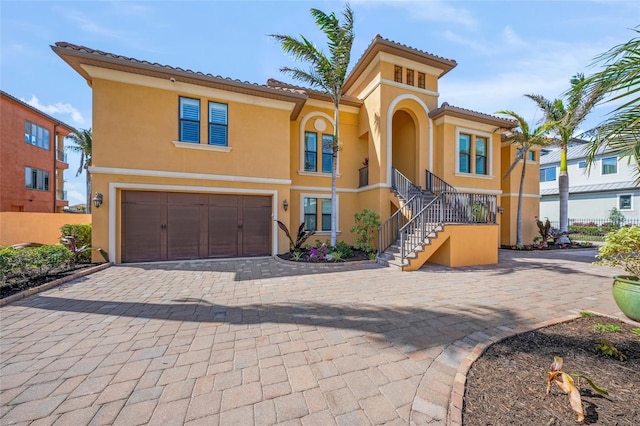 mediterranean / spanish-style house with a tile roof, an attached garage, stairs, decorative driveway, and stucco siding