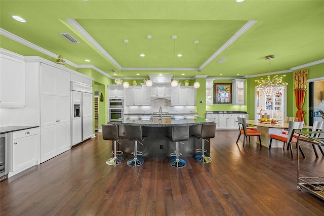 kitchen with paneled built in refrigerator, a tray ceiling, visible vents, and white cabinets