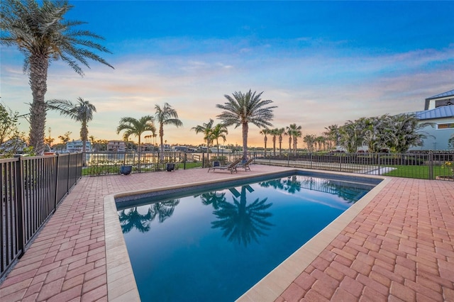 pool at dusk with a patio area, fence, and a fenced in pool