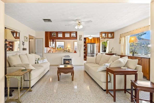 living room featuring visible vents, a textured ceiling, light speckled floor, and ceiling fan