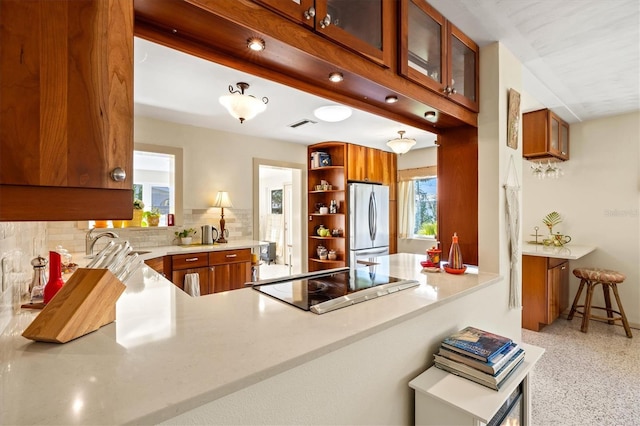 kitchen with black electric cooktop, brown cabinetry, and freestanding refrigerator